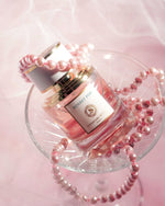 Flacon de parfum Sunset Pop Signature Royale présenté dans une coupe avec des perles roses.